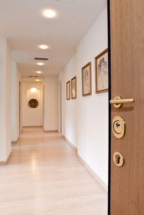 A hallway with wooden flooring, a wooden door with a keyhole, and framed artwork on the wall.