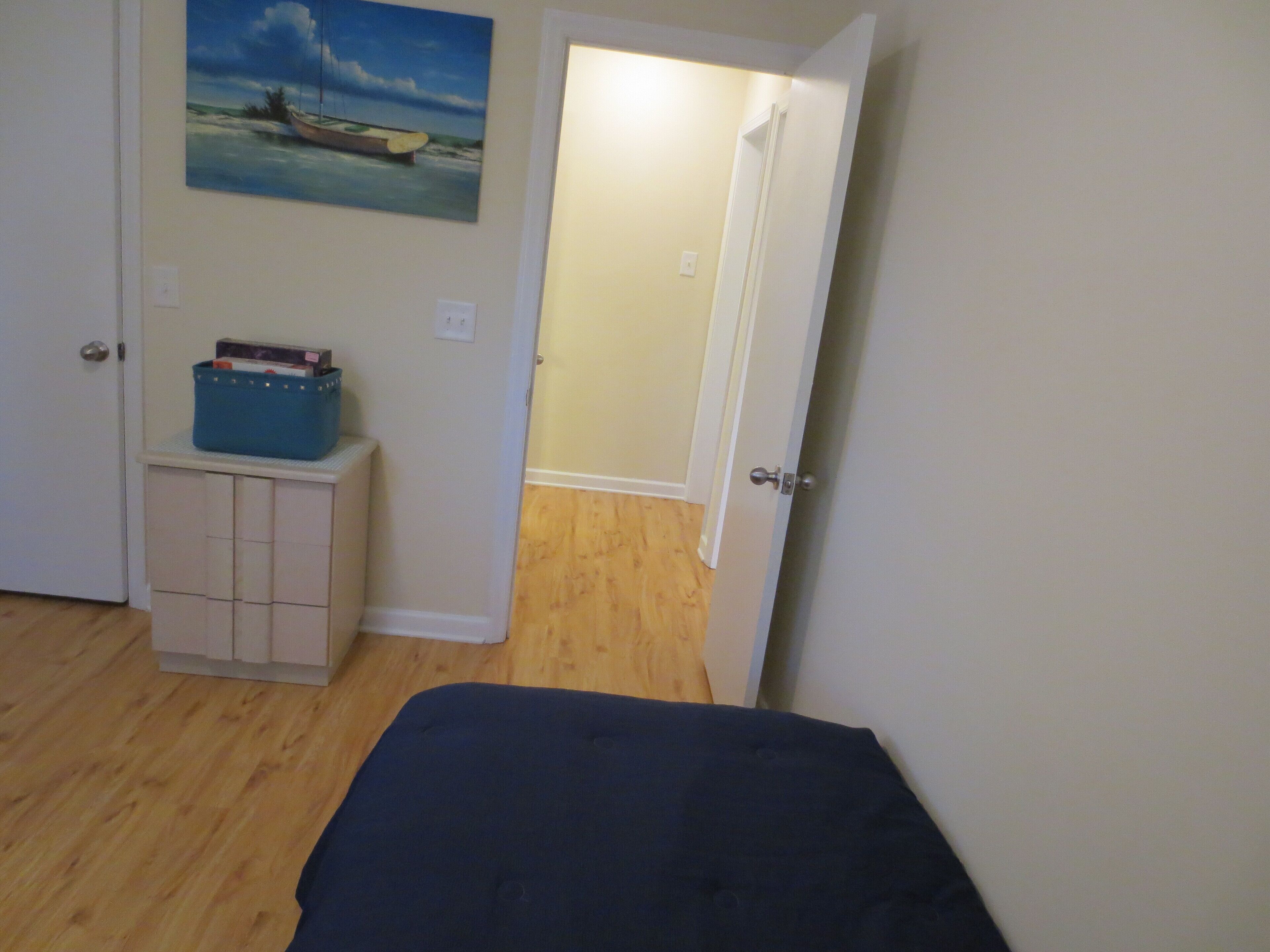 A bedroom with a bed, a dresser, a painting, and an open door leading to another room.