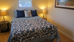 A bedroom with a bed, two bedside lamps, a window with blinds, and a framed picture on the wall. - Apartment In Downtown Durham (Durham)