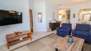 Ein Wohnzimmer mit Flachbildfernseher, blauen Sofas, einem Holztisch und einer Bank.