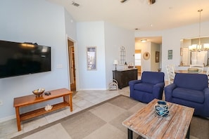 A living room with a flat-screen TV, blue sofas, a wooden coffee table, and a bench.