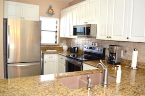 A kitchen with white cabinets, stainless steel appliances, granite countertops, and a window with blinds.