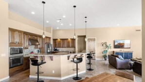 A modern kitchen with a central island, bar stools, and a dining area with a wooden table. - Voted # 1 House-Pool, Pickleball, Golf, Basketball (Scottsdale)
