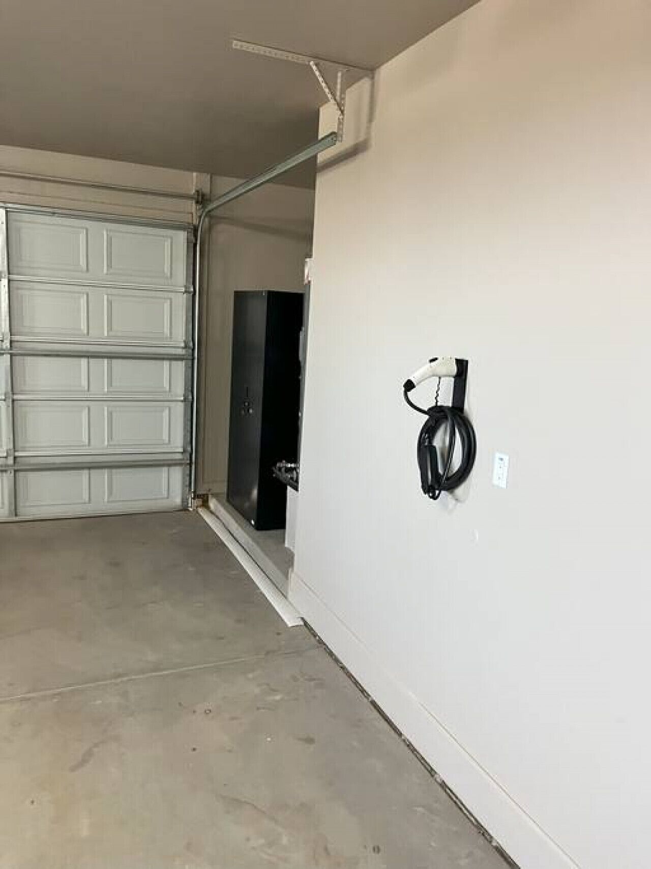 Un garaje con puerta cerrada, una puerta negra y una pared blanca con un cable negro colgando.
