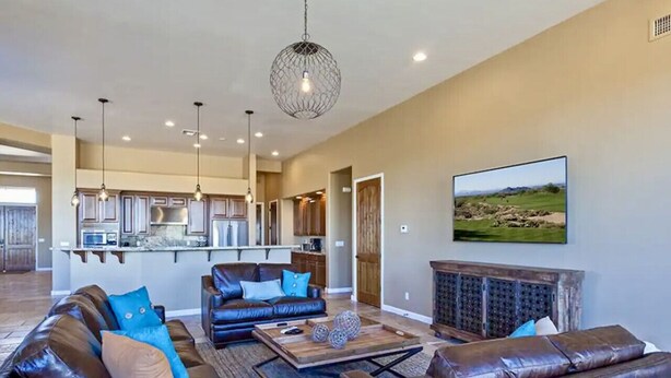 A spacious living area with leather sofas, a coffee table, and a fireplace. A kitchen is visible in the background with modern appliances. - Voted # 1 House-Pool, Pickleball, Golf, Basketball (Scottsdale)