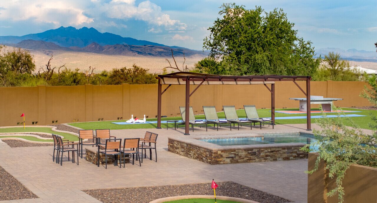 Zona de piscina con sillas de descanso, una mesa y una pérgola.