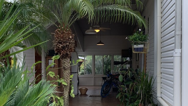 A covered porch with a wooden floor, surrounded by potted plants and a bicycle. - Unbeatable Waterfront Deal: Special Offers on 4BR Luxury Canal Retreat (Welaka)