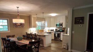 A modern kitchen with white cabinets, a central island, and a dining area with a wooden table and chairs. - Lake Watauga FAMILY FUN, Sunny Lake Front Home  Private Dock  Water Toys WiFi (Butler)