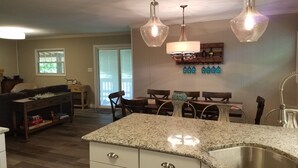 A kitchen with granite countertops, a stainless steel sink, and pendant lighting. There is a dining area with a table and chairs, and a sliding glass door leading to a balcony. - Lake Watauga FAMILY FUN, Sunny Lake Front Home  Private Dock  Water Toys WiFi (Butler)