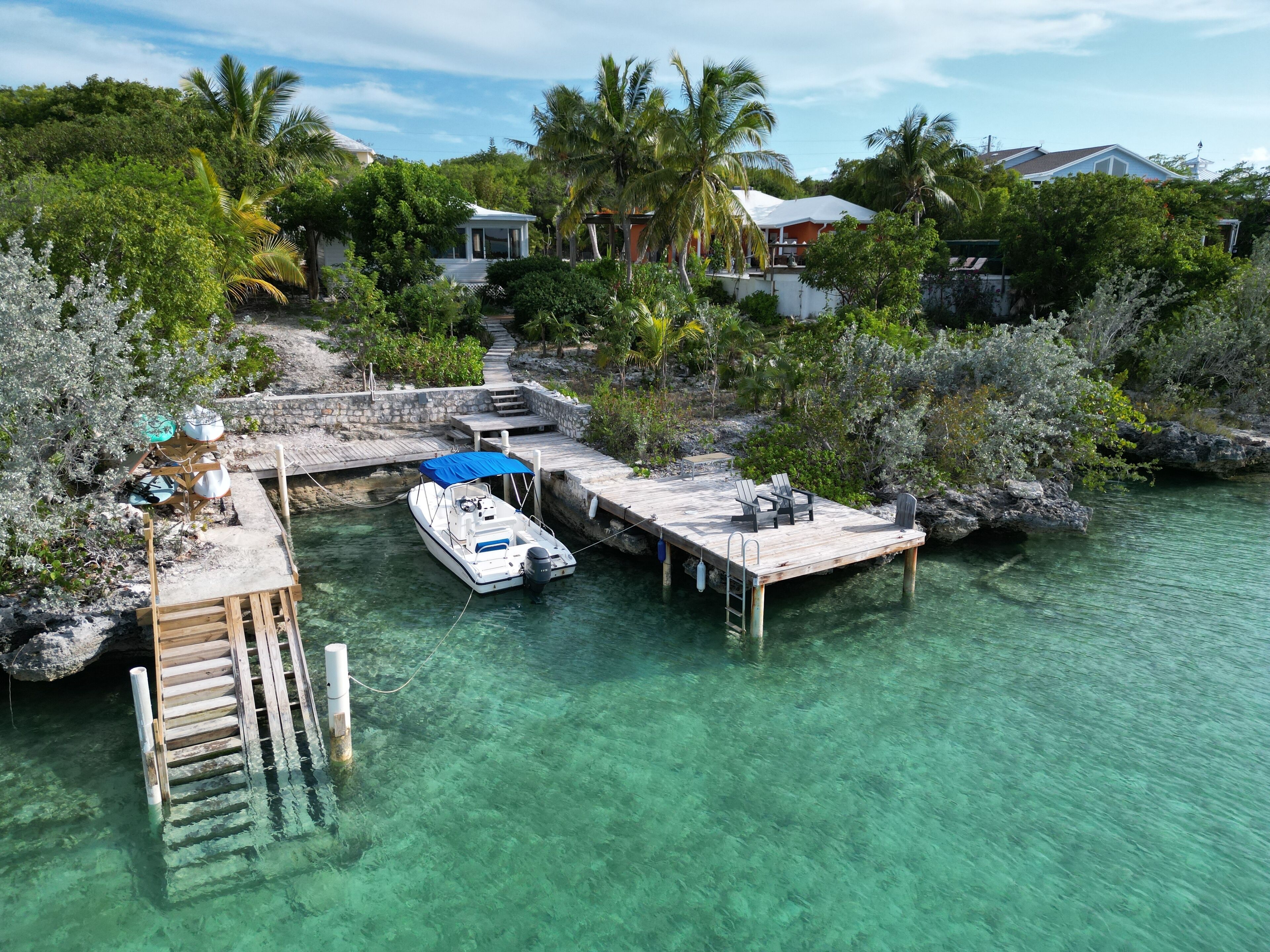 A boat docked at a pier with a wooden walkway leading to a house surrounded by lush greenery.