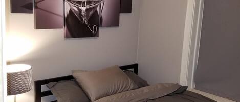 Een slaapkamer met een bed, nachtkastje, lamp en plafondventilator.
