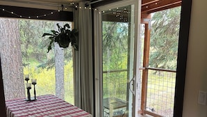 Una habitación con una cama, una mesa con mantel, una planta en maceta y vistas a una terraza de madera y árboles al exterior.