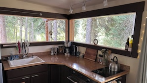 Una cocina moderna con armarios oscuros, un fregadero, una estufa y una ventana con vista a un bosque.