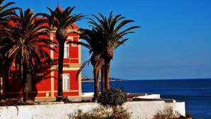 A red building with a white door, palm trees, and a clear blue sky. - Ground floor townhouse, near tourist attractions, water parks (Armação de Pêra)