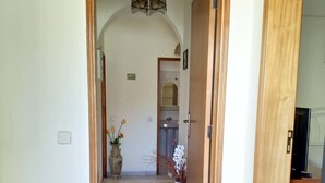 A hallway with a wooden door leading to a bathroom, a small table with a lamp, and a potted plant. - Ground floor townhouse, near tourist attractions, water parks (Armação de Pêra)