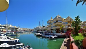 Un port de plaisance où sont amarrés de nombreux bateaux, un ciel d’un bleu limpide et un bâtiment doté d’un style architectural particulier.