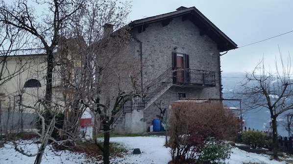 A stone building with a balcony, surrounded by bare trees and snow.