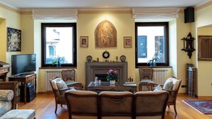 Un salon avec une cheminée, des meubles en osier, un téléviseur et des œuvres d’art accrochées aux murs.