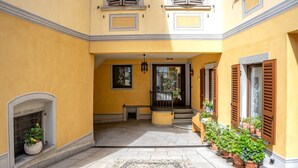 Un bâtiment jaune avec une cour dallée, une cheminée et des plantes en pot.