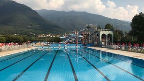 Une piscine à l’eau cristalline, entourée de montagnes, avec un parc aquatique en arrière-plan.