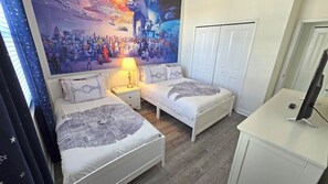 Un dormitorio con dos camas, una mesita de noche, un escritorio y un amplio mural con temática espacial en la pared.