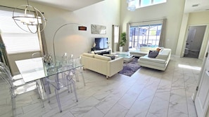 A modern living room with a glass dining table, white sofas, and a flat-screen TV.