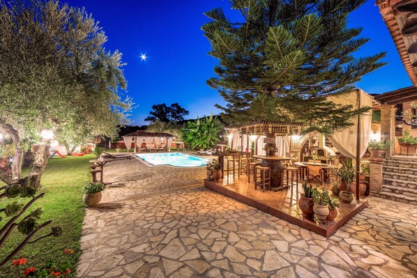 A stone patio with a pool, outdoor furniture, and potted plants.