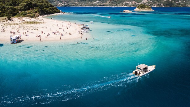 En strand med klart turkis vand, en båd og et redderhus.