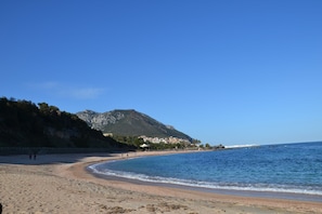 A beach with a mountain in the background, clear skies, and a few people walking.