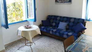 Ein Zimmer mit einem blau gemusterten Sofa, einem kleinen runden Tisch mit weißem Tuch und einem Segelbootsbild an der Wand.