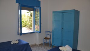 Ein Zimmer mit zwei Betten, einem Fenster, einem Sessel und einem Kleiderschrank.