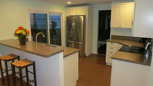 Cocina con armarios blancos, refrigerador de acero inoxidable, encimera de granito y ventana con vistas.