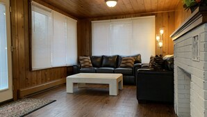 Un salón acogedor con techo de madera, un sofá de cuero negro, una mesa de centro blanca y una chimenea.