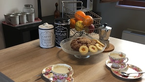 A kitchen counter with a coffee maker, a fruit basket, and a coffee station with cups and saucers.