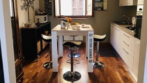 A modern kitchen with a central island, bar stools, a coffee station, and a view of the city through a window.