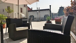 An outdoor seating area with wicker furniture, a large umbrella, and potted plants.