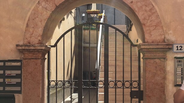 An arched entrance with a metal gate, a number '12' sign, and a mailbox.