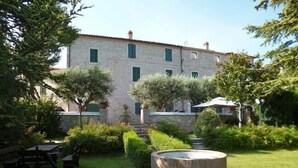 A courtyard with a stone fountain, a stone building with green shutters, and a bench. - Villa La Panoramica (late 18th-century mansion) suitable for large groups. (Cingoli)