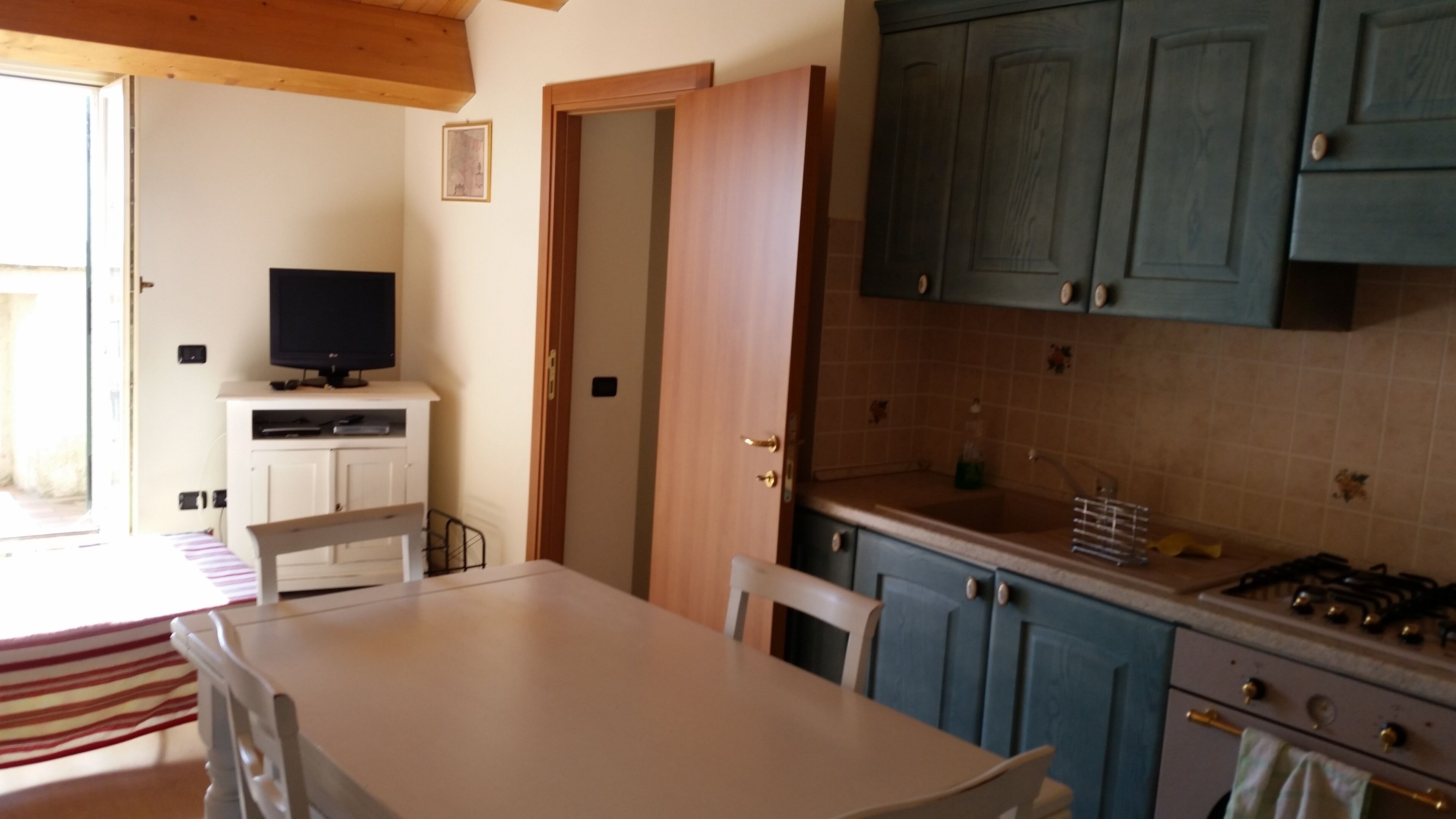 A kitchen with a dining table, chairs, a TV, and cabinets.