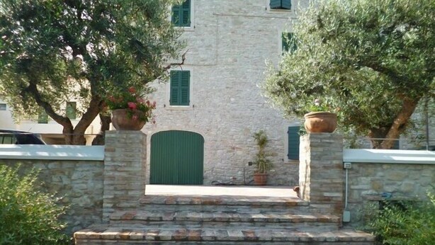 A stone staircase leading to a building with a green door and windows, surrounded by greenery and potted plants. - Villa La Panoramica (late 18th-century mansion) suitable for large groups. (Cingoli)