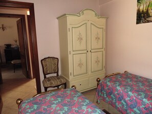Ein Schlafzimmer mit zwei Betten, einem Holzschrank, einem Stuhl und einem Bild an der Wand.