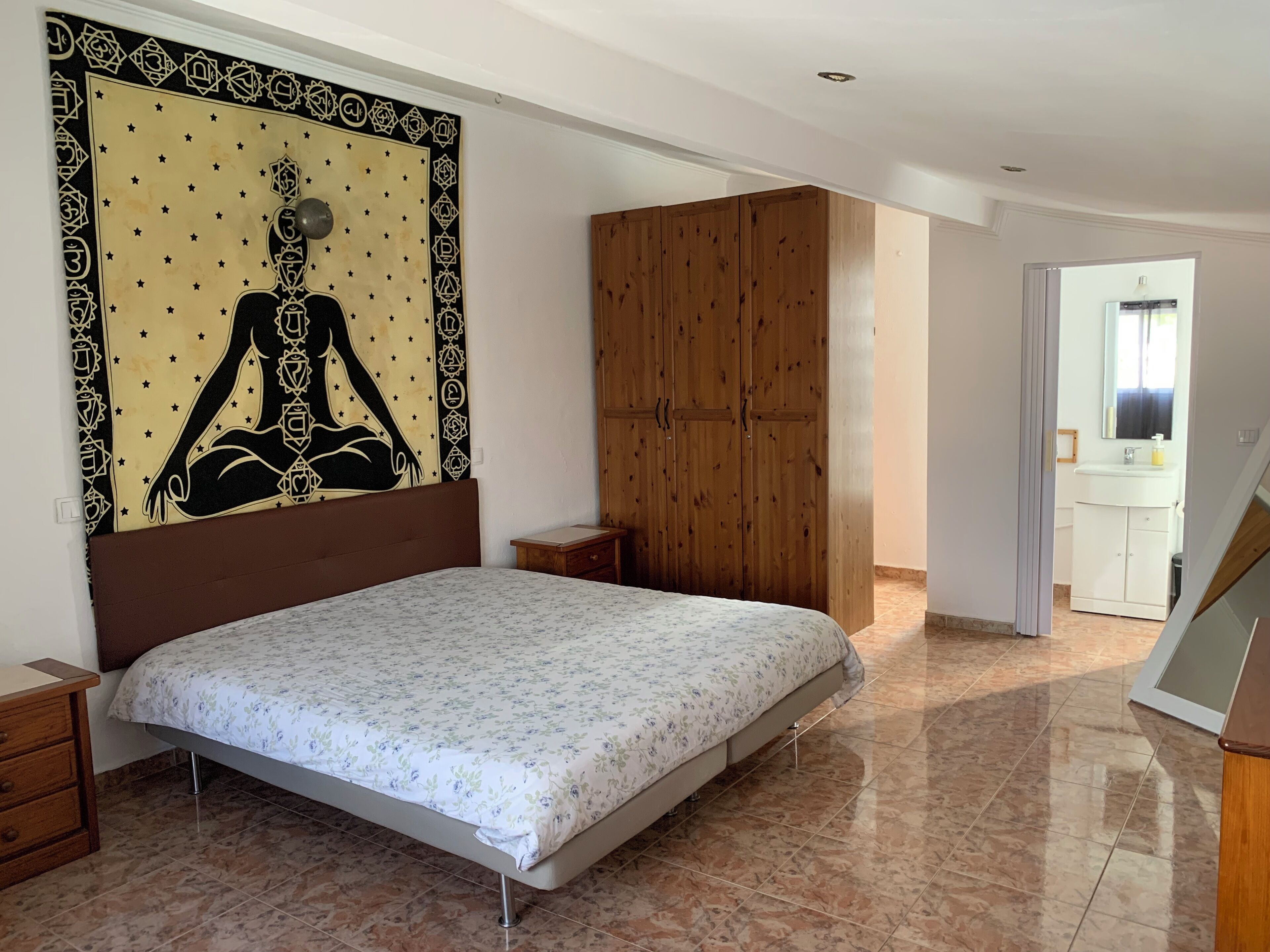 A bedroom with a bed, wooden wardrobe, and a tapestry on the wall.