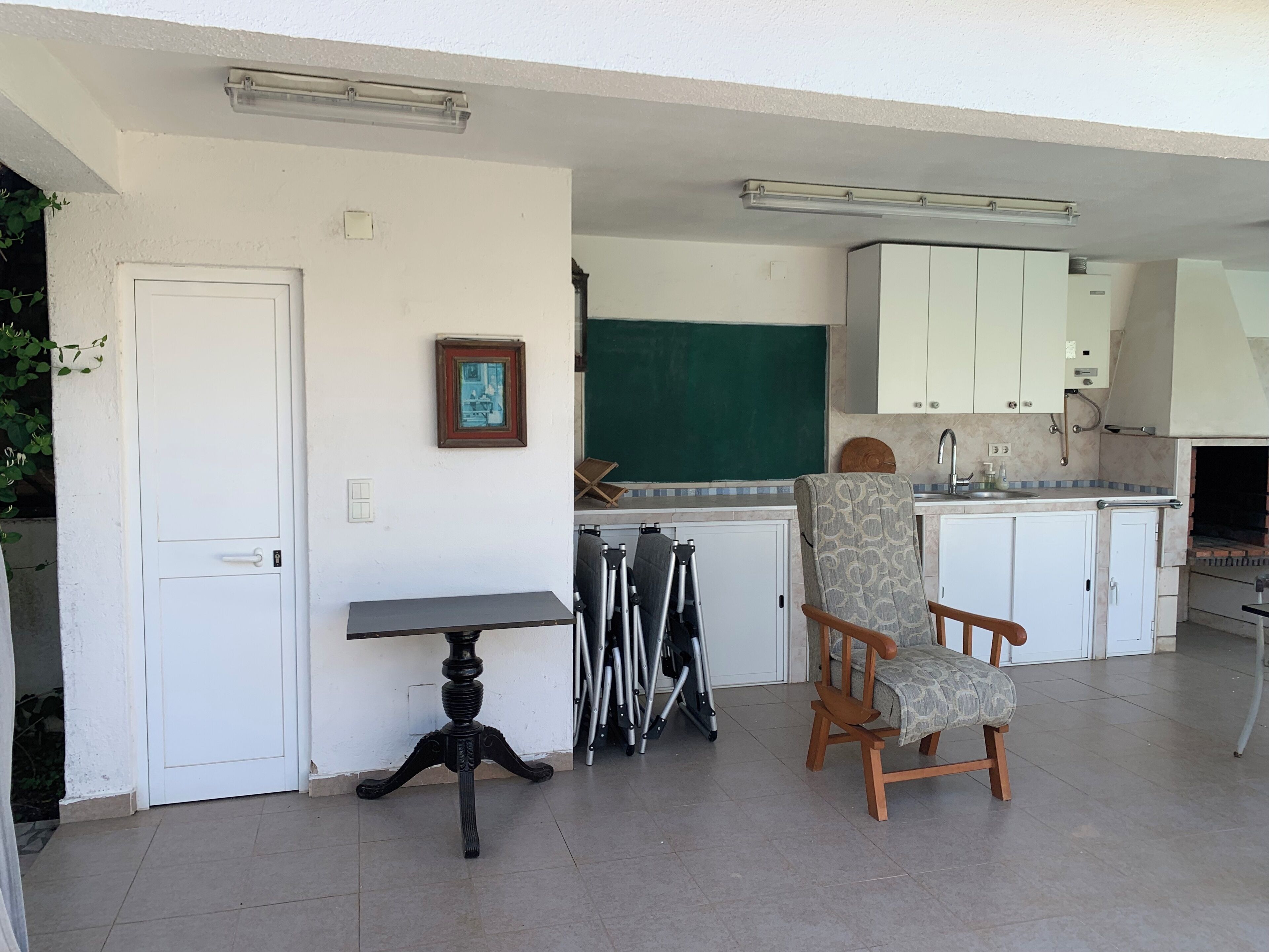 Una cocina compacta con armarios blancos, una pizarra verde y un pequeño comedor con mesa y sillas.