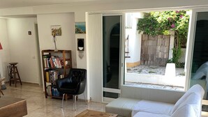 A living room with a white sofa, a wooden coffee table, a black leather chair, a bookshelf, and a sliding glass door leading to an outdoor area. - AroeiraMIR - Villa with private pool and garden, Lisbon South Bay [38274 / AL] (AROEIRA)