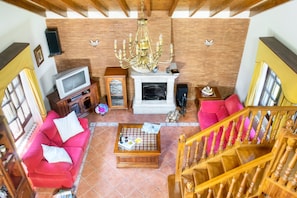 A spacious living room with a red sofa, a wooden coffee table, a fireplace, and a staircase.