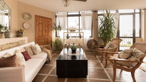 Ein Wohnzimmer mit einer Couch, Sesseln, einem Couchtisch und einem großen Fenster mit Vorhängen.