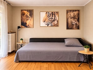 A bedroom with a bed, a radiator, a small table with a plant, and three framed animal paintings on the wall.