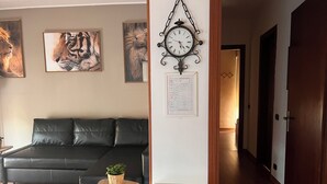 Ein Wohnzimmer mit einem schwarzen Ledersofa, einem kleinen Holztisch mit einer Pflanze, einer Wanduhr und gerahmten Tierbildern.