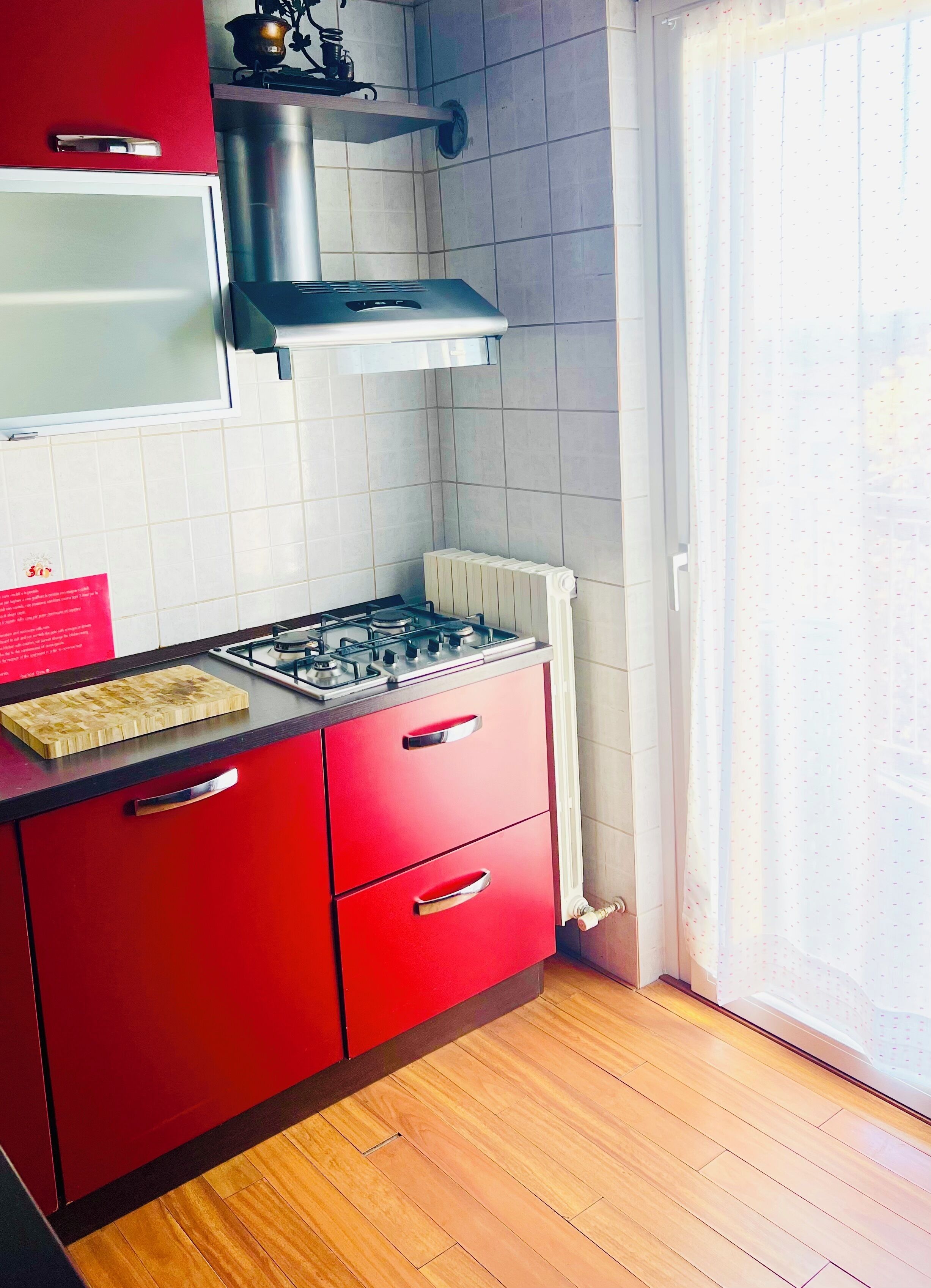 A kitchen with a gas stove, red cabinets, a wooden countertop, and a window with a view.