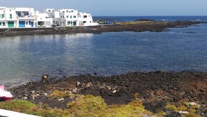 A coastal area with white buildings, a rocky shoreline, and calm water. - Odamar Órzola apartament (Órzola, Lanzarote)